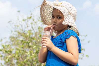 Portrait of young woman drinking water while standing against trees