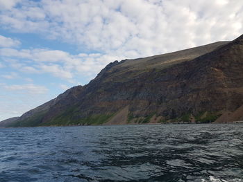 Scenic view of sea by mountain against sky