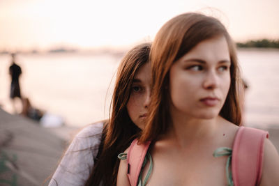 Portrait of lesbian couple sitting by river at sunset during summer