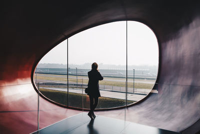 Rear view of woman standing against glass window