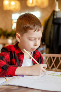 Handsome little boy draws at the table with a pencil. waiting for an order in a cafe. the boy draws 