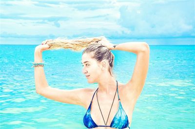 Beautiful woman playing with long blond hair at beach against blue sky