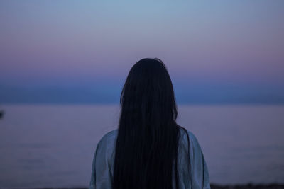 Rear view of woman standing against sea at sunset