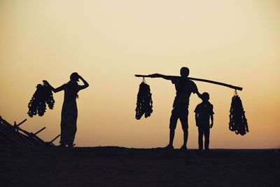 Silhouette people standing on beach against clear sky during sunset