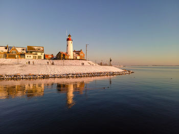 Reflection of lighthouse on building by sea against clear sky