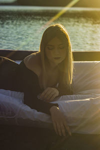 Young woman lies putting his hand down a mattress on the water and the sunset illuminates her hair