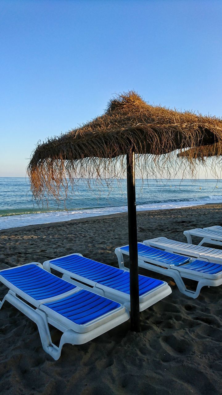 LOUNGE CHAIRS ON BEACH AGAINST CLEAR BLUE SKY