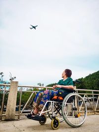 Woman sitting on wheelchair against airplane in sky