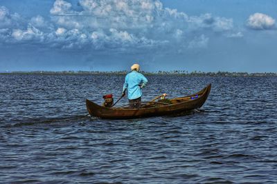 Rear view of man sailing on sea against sky