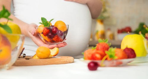 Midsection of pregnant woman with bowl of fruits