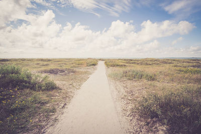 Dirt road on field against sky