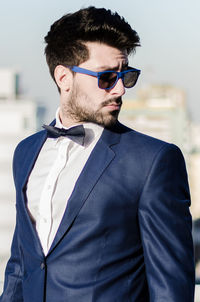 Young man wearing suit and sunglasses standing against sky