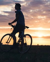 Silhouette boy riding bicycle against sky during sunset