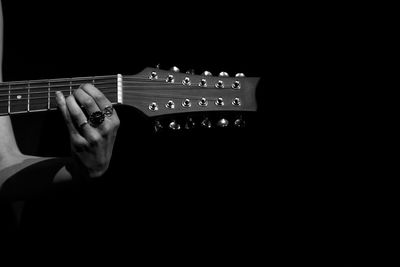 Cropped hand of woman playing guitar against black background