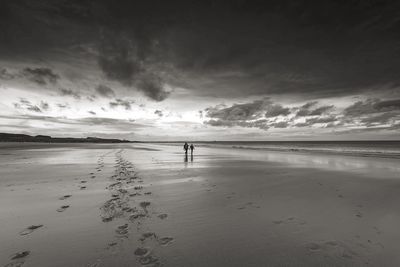 People walking on sand against sea during sunset