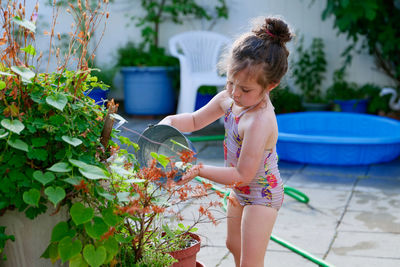 Cute young girl watering plants with a bucket on a summer day in the backyard