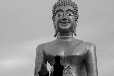 Rear view of couple standing against buddha statue against sky