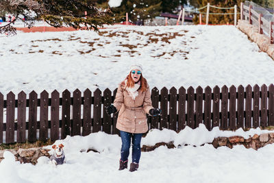 Cheerful woman carrying dog while standing on snowy land