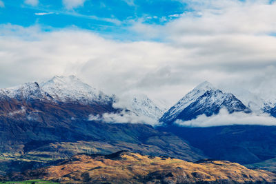 Scenic view of snowcapped mountains against cloudy sky on sunny day