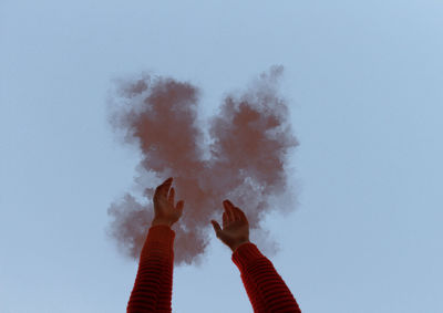Cropped hand amidst smoke against sky
