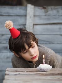 Birthday boy in grey knitted sweater with dark short hair blows candle on the birthday cake