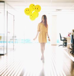 Full length of young woman standing by balloons in office