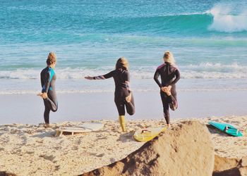 Rear view of surfers exercising on sand at beach