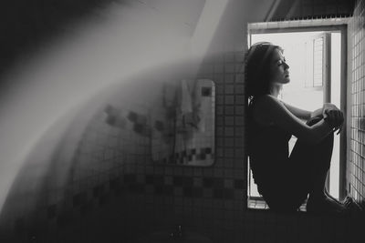 Side view of mid adult woman sitting on window at home