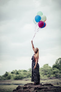 Rear view of woman with balloons standing on rock