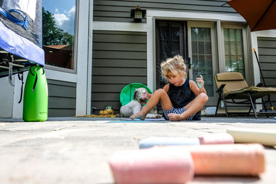 Girl sitting on ground in backyard playing with chalk