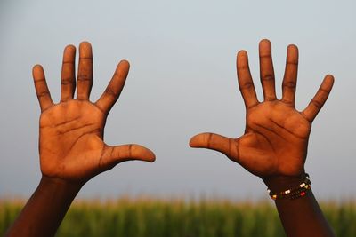 Cropped hands of person showing stop gesture against sky