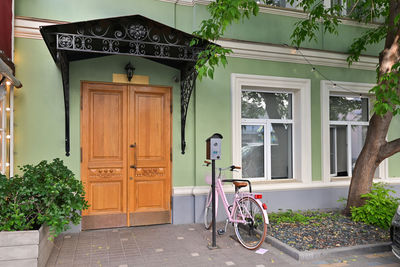 An entrance with a wooden brown door of an apartment building and a parked pink bicycle.
