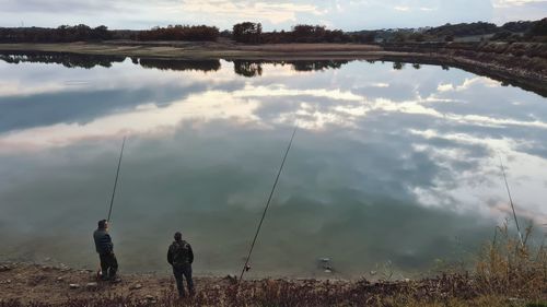 People fishing in lake against sky