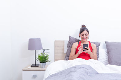 Young woman using mobile phone while sitting on bed at home