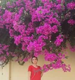 Portrait of smiling young woman standing by pink flowering plants against wall