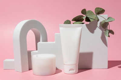 White blank cosmetic product bottles on pink background with eucalyptus branch, as advertisement. 