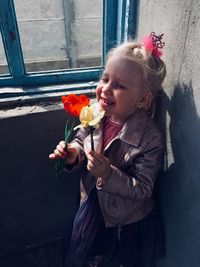 Girl holding flower while standing against wall