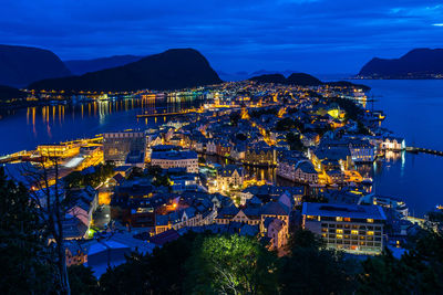 High angle view of illuminated city by sea against sky at dusk