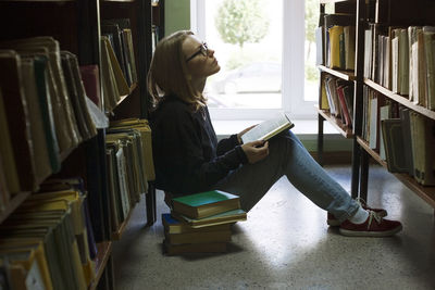 Woman holding book and looking up while sitting in library