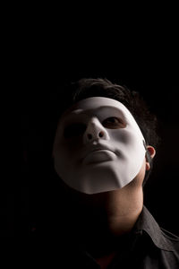 Close-up of man wearing mask against black background