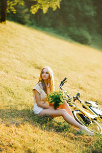 Portrait of a beautiful girl in the forest, sitting on the grass, next to a bicycle, with a bouquet 