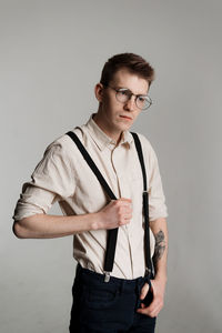 Young man wearing suspenders standing against white background