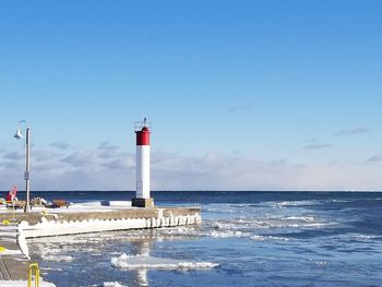 Lighthouse by sea against blue sky