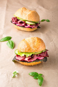 Ready-to-eat hamburgers with pastrami, cucumber, radish and herb on craft paper.