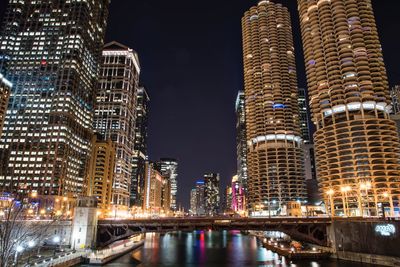 Illuminated buildings by river against sky at night