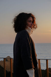 Side view of woman standing by railing against sea during sunset