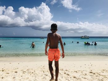 Rear view of boy standing at beach against sky