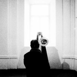 Rear view of woman photographing against wall at home