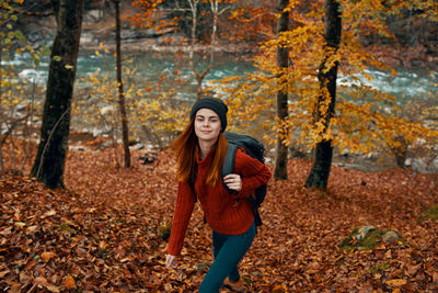 Portrait of young woman standing with autumn leaves in forest