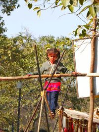 Full length of skilled girl holding bamboo while walking on rope outdoors